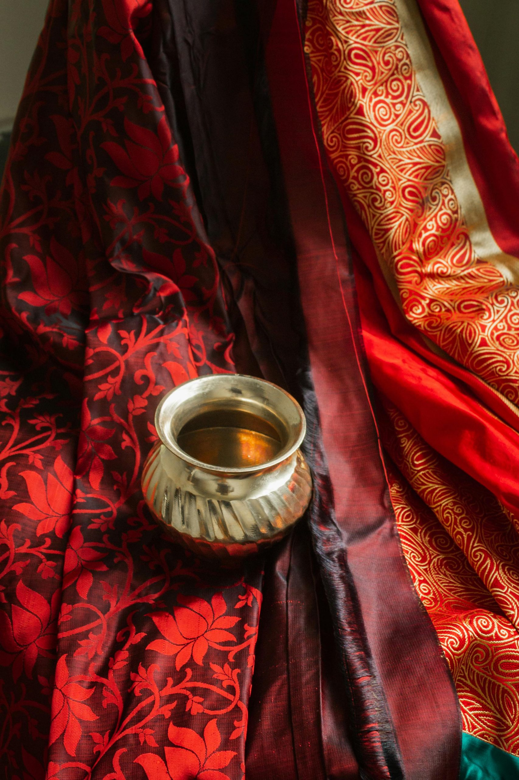 A traditional Indian brass bowl set against rich, decorative red and gold fabrics in Varanasi.